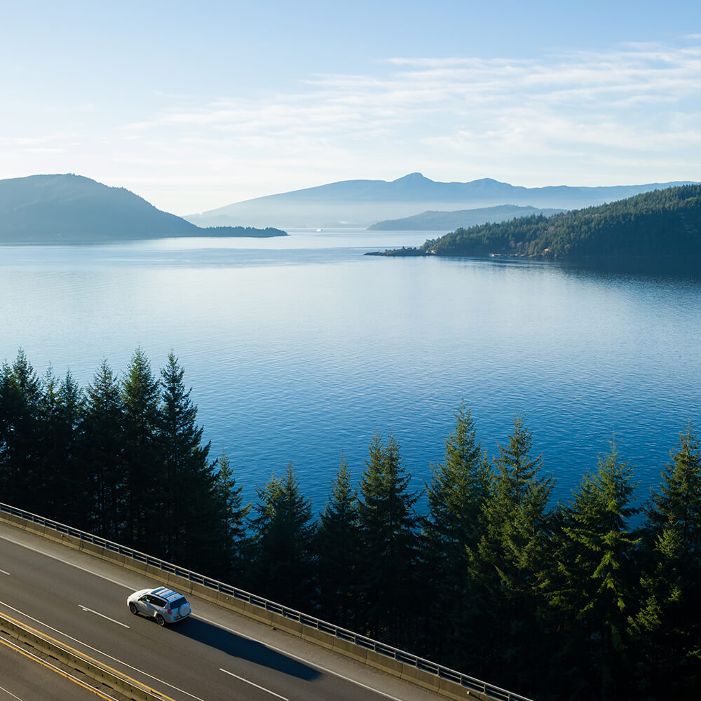 a lone vehicle traveling the sea to sky highway with the Sunshine Coast in the distance