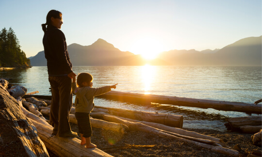 Mother and daughter standing on a beach looking out at the ocean on the BC coast.